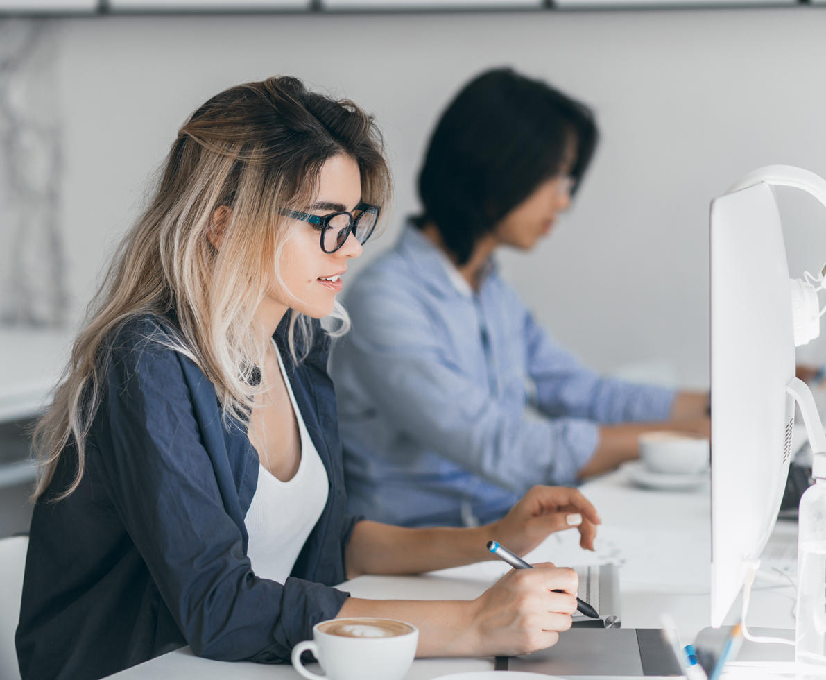 Busy female freelancer with long hair working with tablet and drinking coffee